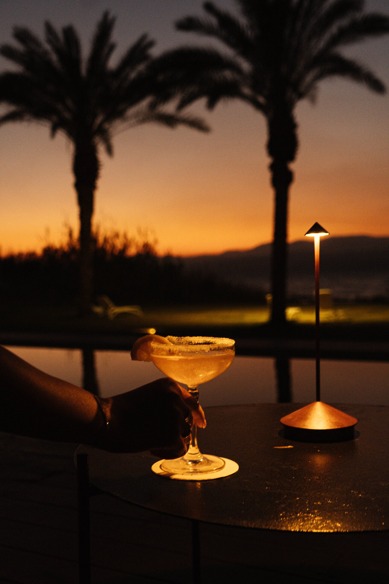 A cocktail on the pool edge at sunset, palms against the sky